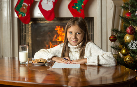 快乐的笑女孩坐在壁炉边写给圣诞老人的信图片