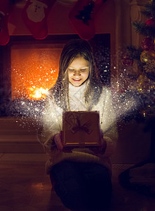 快乐的笑女孩打开闪亮的圣诞礼物盒灯光和火花从盒子里飞出来背景图片