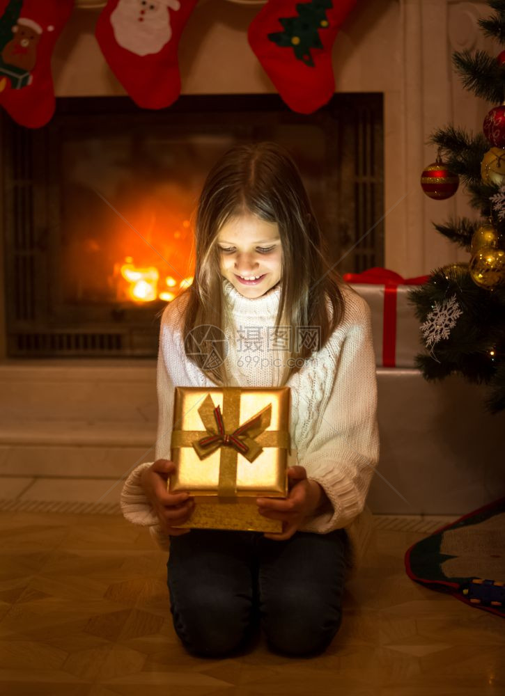 带着圣诞礼物的开心女孩打盒子光亮闪的光从盒子里出来图片