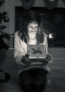 女孩坐在壁炉的地板上打开圣诞礼物盒图片