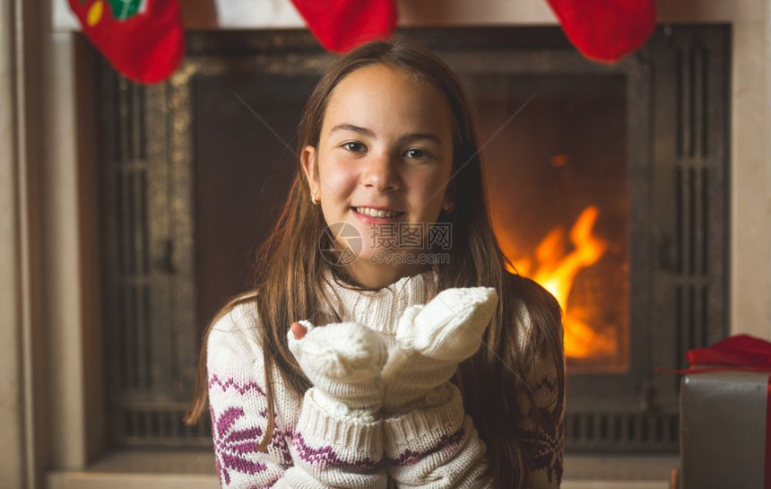 坐在壁炉边从手中吹雪的可爱少女肖像图片