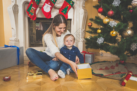母亲和婴儿在地板上微笑看着圣诞礼物图片