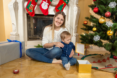 男孩宝和母亲在客厅的圣诞树下打开礼物盒图片
