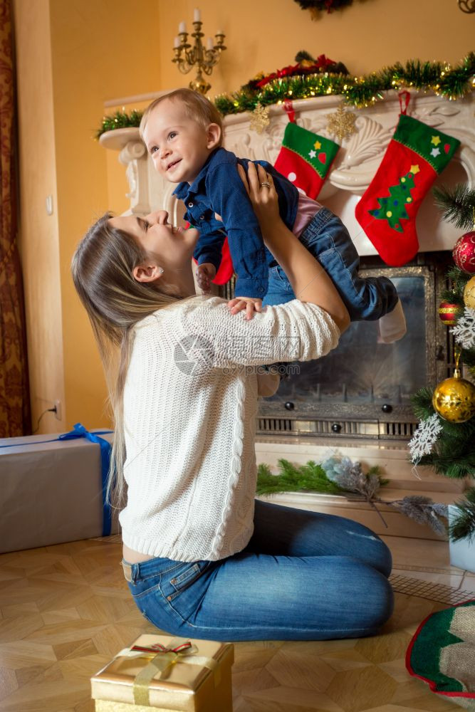 幸福的母亲在圣诞树上与她一岁大的儿子玩耍图片