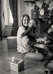 快乐的年轻母亲在圣诞树上拥抱她一岁小男孩的黑白像图片
