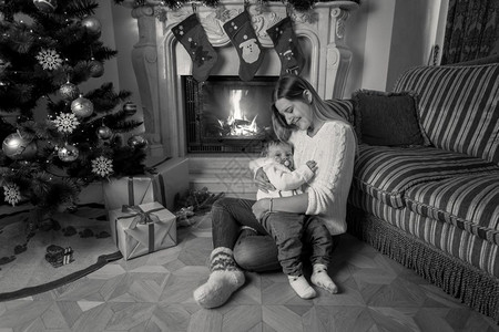 美丽的年轻母亲黑色和白画面她的婴儿男孩一起坐在壁炉旁边圣诞节的壁炉旁图片