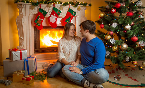 坐在燃烧的壁炉上送圣诞礼物的年轻夫妇图片