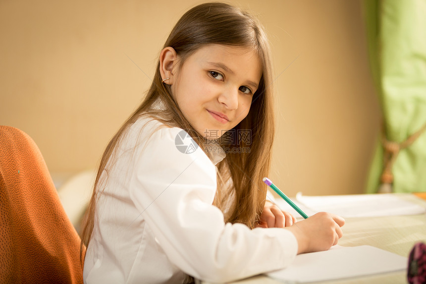 穿着白衬衫坐在桌后做功课的笑着黑头发女孩肖像图片