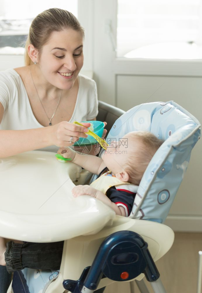 年轻母亲喂养坐在高椅子上的男婴图片