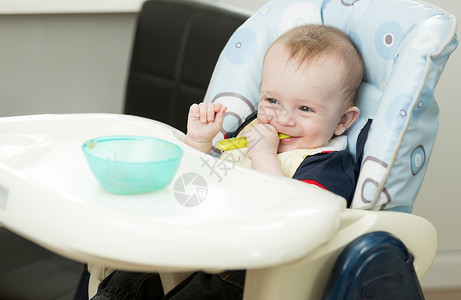 婴儿男孩坐在高椅子上玩勺和盘高清图片
