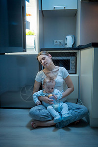 睡着的年轻母亲坐在厨房里与她儿子坐在冰箱旁边的图片