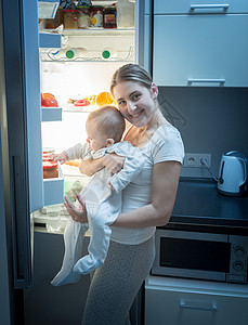 微笑的女人与她儿子一起在夜间厨房的里站着图片