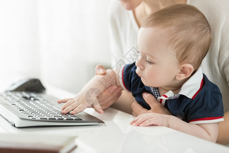 年轻母亲坐在电脑上抱着婴儿在大腿上图片