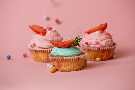 三个彩色纸杯蛋糕粉红背景的草莓彩色糖果图片