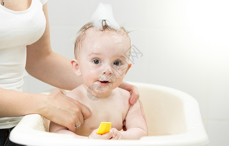 一起洗澡的婴儿与黄橡皮鸭一起在泡浴中玩的可爱男孩背景