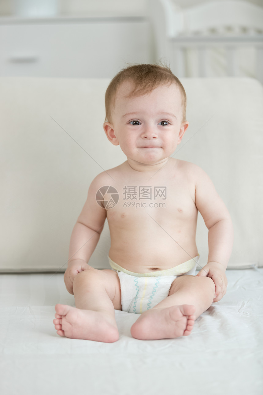 坐在床上和手持智能机的尿布中婴儿男孩图片