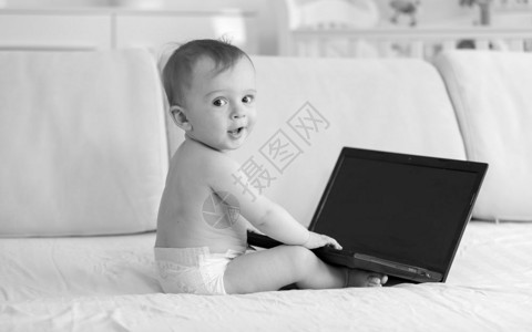 坐在沙发上并使用笔记本电脑的1岁婴儿男孩黑白画面图片