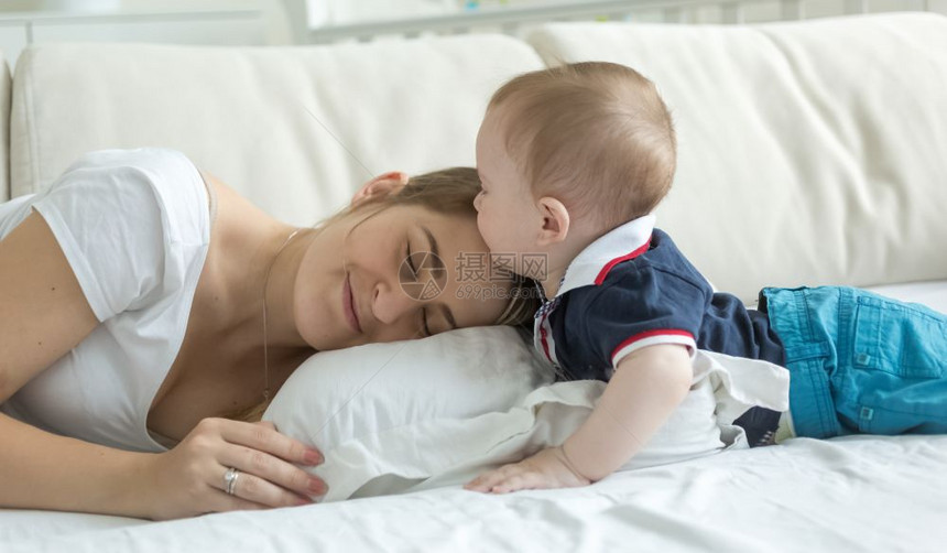 年轻母亲躺在床上与婴儿互动图片