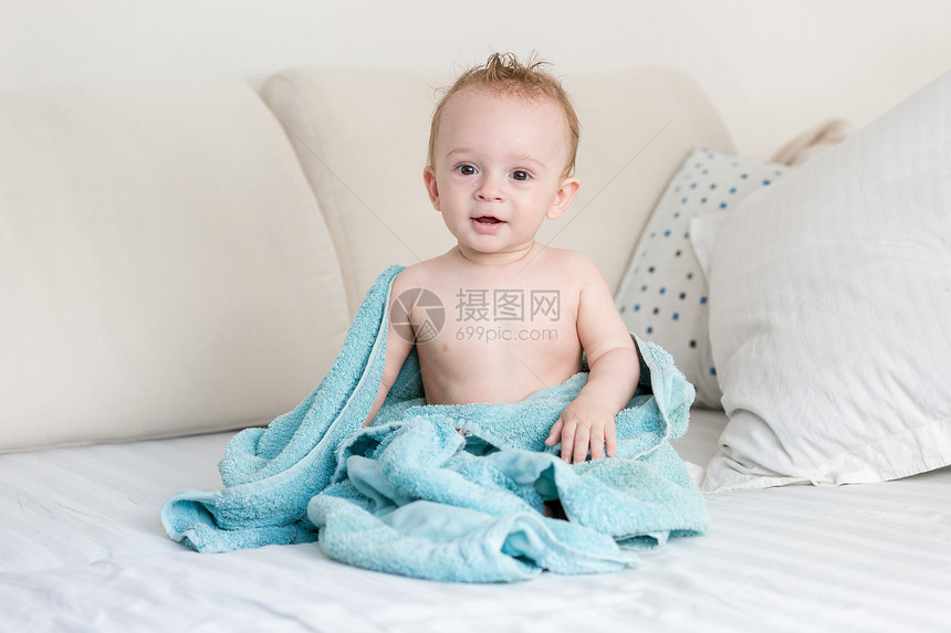 穿着蓝毯子坐在床上的可爱男孩图片
