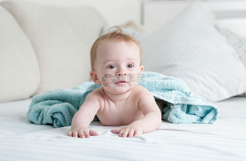 9个月大的婴儿在洗完澡后穿着蓝毛巾爬在床上图片