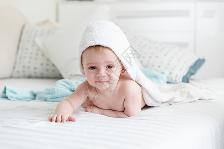 穿着毛巾的婴儿男孩洗澡后在床上爬图片