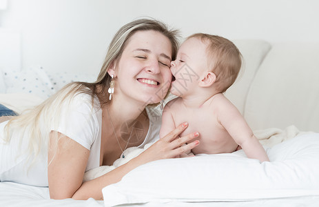 快乐的母亲抱和吻在床上的婴儿男孩肖像背景图片