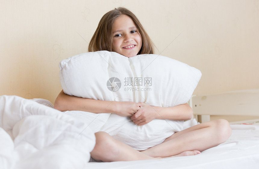 美丽的黑发女孩肖像坐在床上带着白枕头的图片