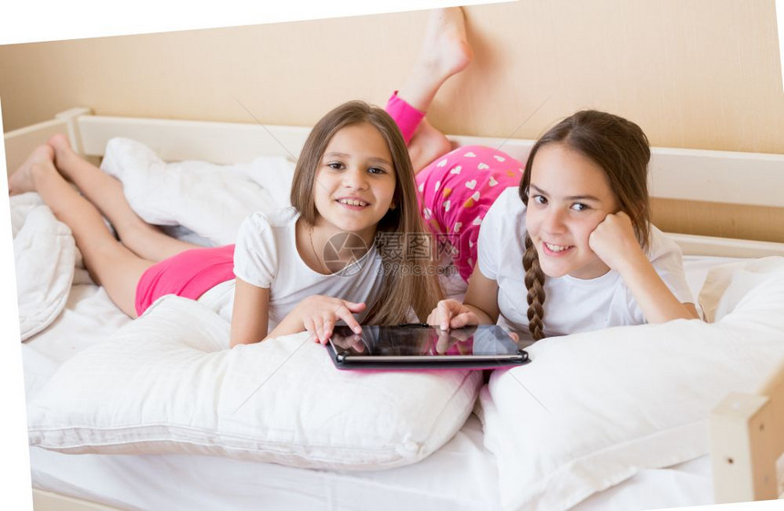 两个快乐的少女躺在床上使用数字平板电脑图片