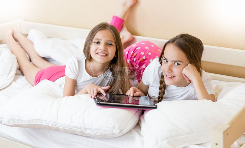 每天早上在床使用平板电脑对两个少女姐妹的肖像图片