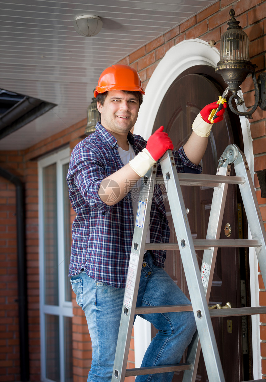男电工在硬帽站起继板和修理房屋灯图片