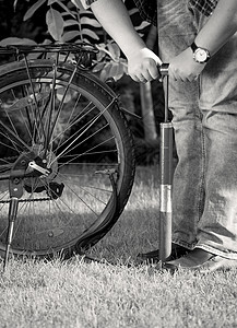 青年男子用手动泵自行车轮胎的黑白照片图片
