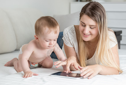 微笑的母亲看着她孩子在平板电脑上玩耍图片