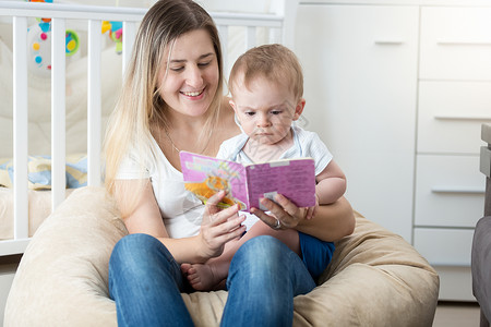 美丽的年轻母亲在大腿上抱着婴儿和阅读书图片