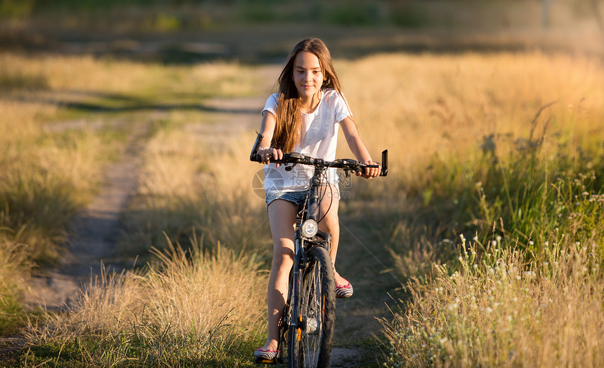 日落时在草地骑自行车的微笑女孩图片