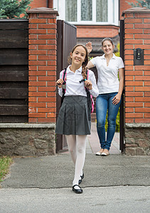 微笑的女孩走出家门上学母亲站在门口向她挥手图片