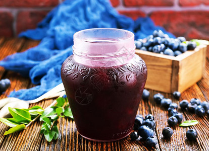 蓝色罐子蓝莓果酱在玻璃库和一张桌子上背景