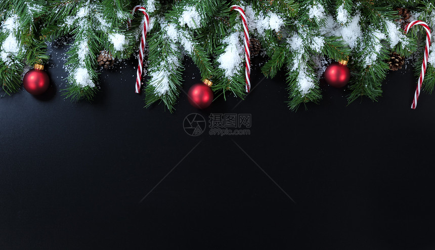 黑色背景的雪圣诞树枝糖果甘蔗和红装饰品图片