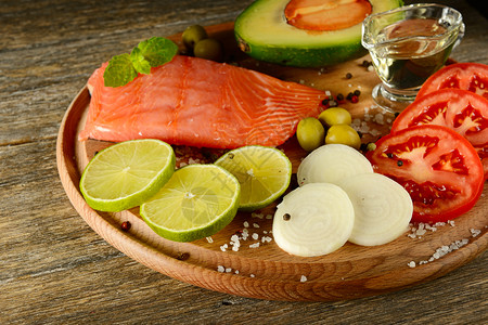 生锈厨房木板上的新鲜蔬菜和熏鱼鲑石灰洋葱橄榄番茄和油以前景为重点图片