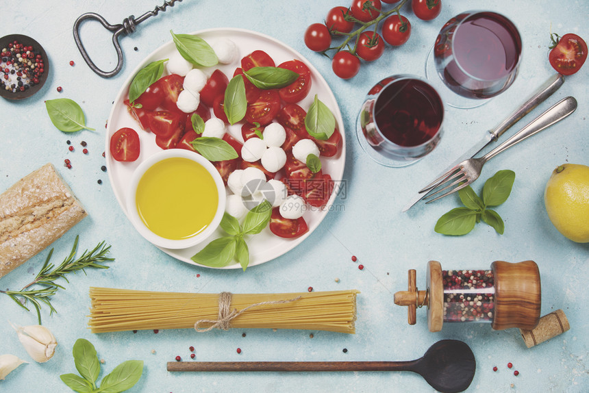 意大利食物背景莫扎雷拉奶酪新鲜的巴西叶番茄橄榄油意大利面条和红酒杯放在混凝土背景顶视线上图片