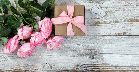 五打粉红玫瑰和礼物盒放在平面的生锈白木上图片