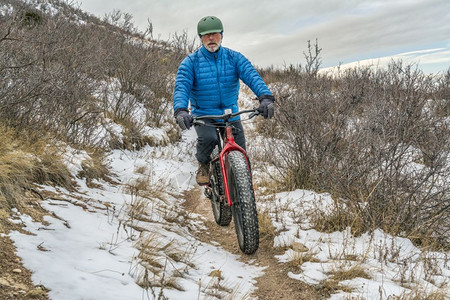 一名高级男骑着肥自行车在CheyenneRim的CheyenneRim红山开放空间秋末或冬季风景和一些雪背景图片