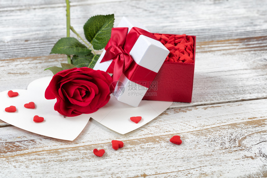 开放的情人节礼物箱里面装满糖果和一朵红玫瑰贴近生锈白木图片