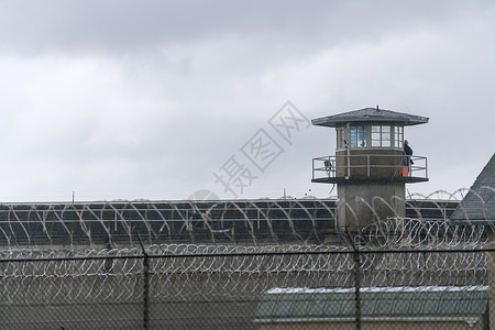 一名武装警卫从个监狱守望塔的栏杆上对地面进行勘察图片