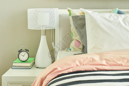 带条纹的床铺旁边时钟和白桌灯背景图片