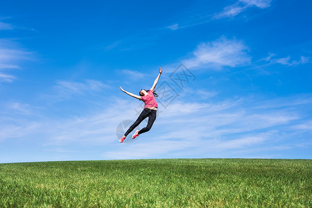 美丽的年轻女跳上绿草地青坪蓝天图片