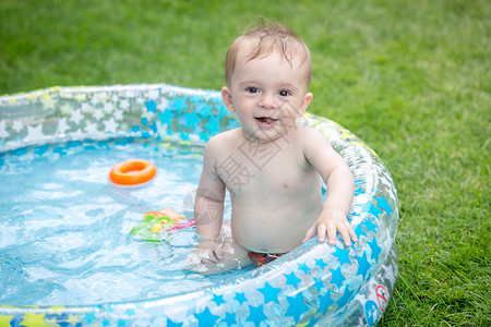 令人愉快的橡胶坐在花园的充气游泳池里坐在花园的充气游泳池里笑的男孩子坐在花园的充气游泳池里背景