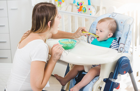 10个月大的婴儿男孩坐在高椅子上吃勺里的粥高清图片