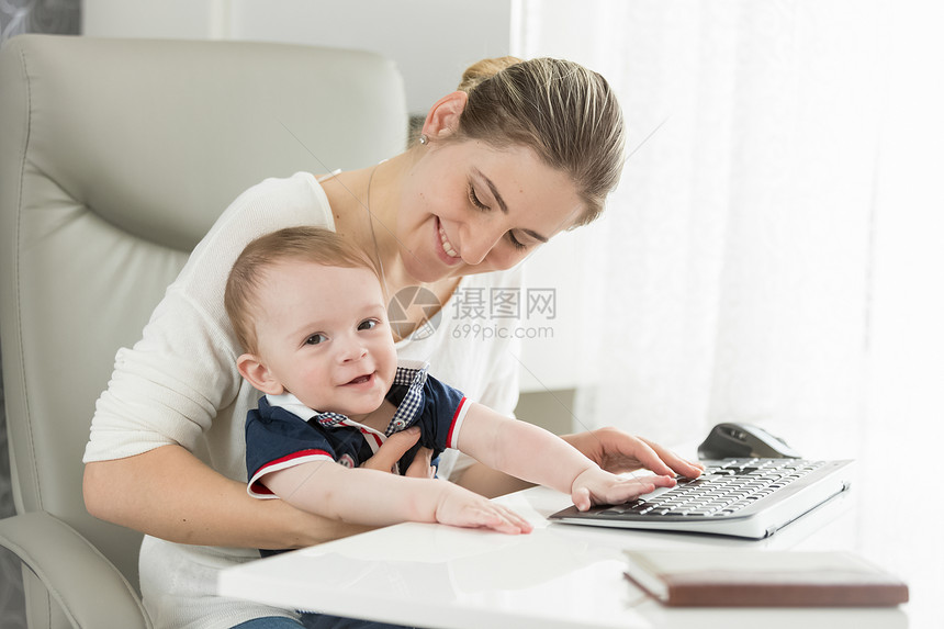 快乐的母亲孩子儿坐在家庭办公室的桌后快乐的母亲和孩子儿坐在家庭办公室的桌后图片