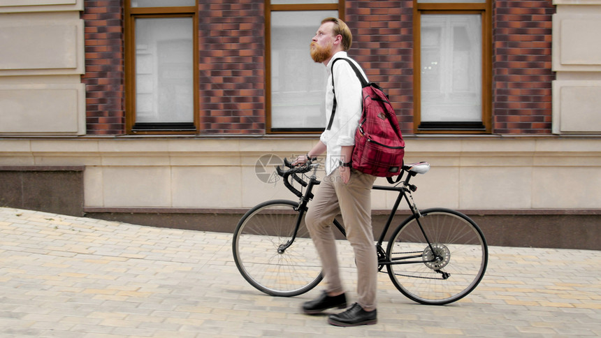 留着络腮胡须的男子推着自行车在城市街道上图片