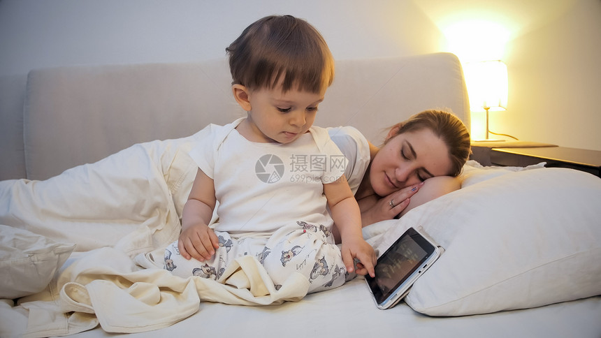小可爱男孩在母亲睡床上时使用数字平板电脑小男孩在母亲睡床上时使用数字平板电脑图片